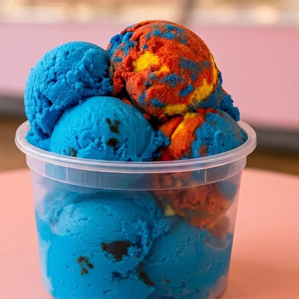 A clear plastic cup filled with scoops of bright blue and multicolored orange and yellow ice cream.