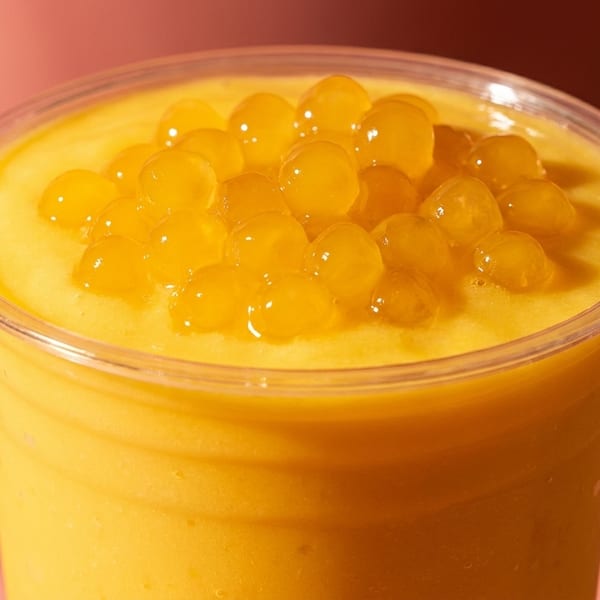 Close-up of a mango smoothie in a clear plastic cup, topped with golden popping boba.